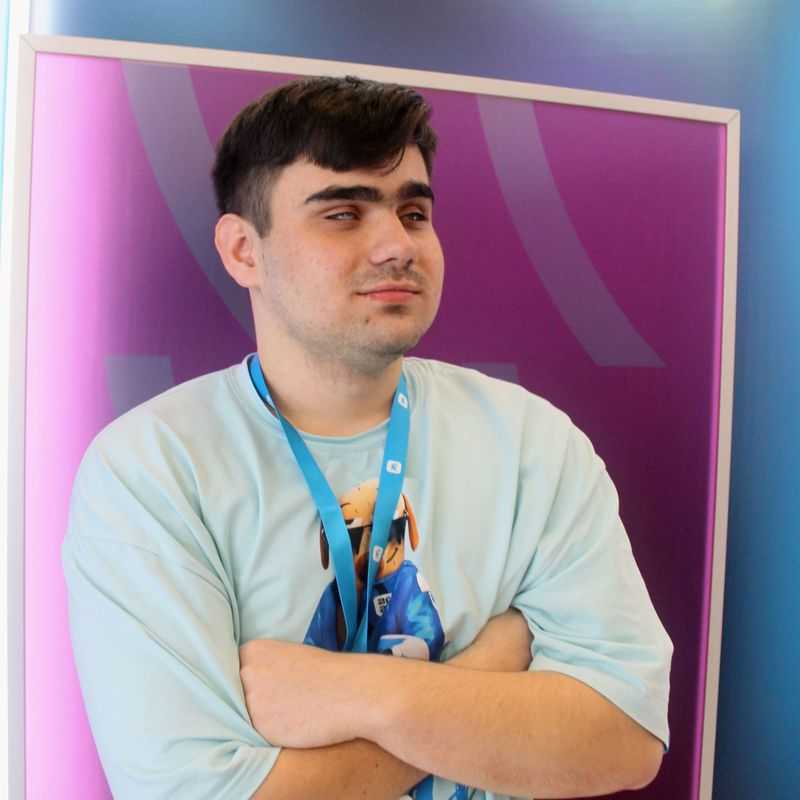 Молодой мужчина с тёмными волосами, сидит перед ярким фоном